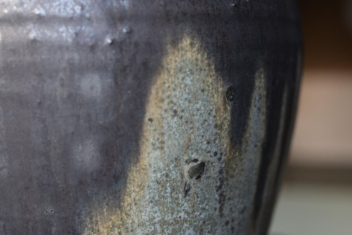 A close-up view of a textured ceramic vase or pot, with a dark gray or black color and a speckled or speckled pattern.