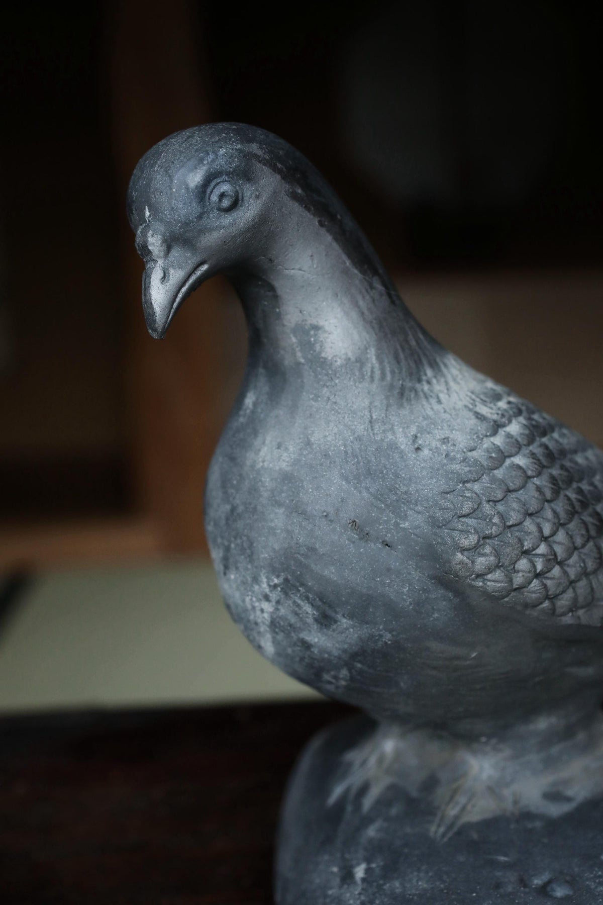 A close-up view of a weathered, gray metal bird statue perched on a rock.
