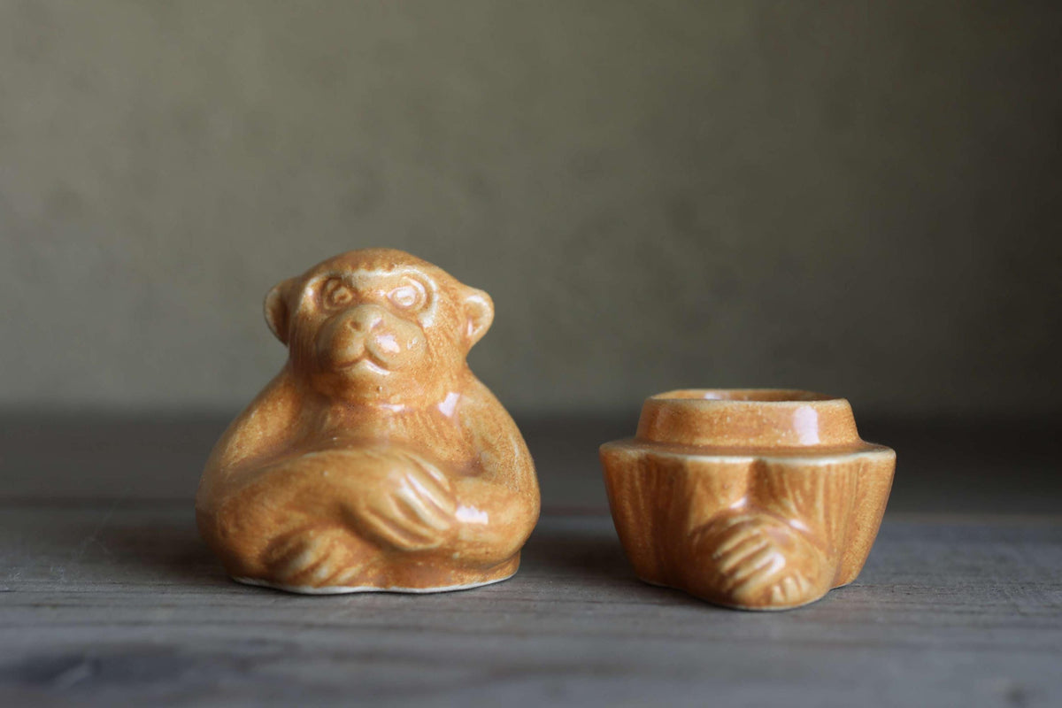 Two ceramic figurines of a monkey sitting on a wooden surface.