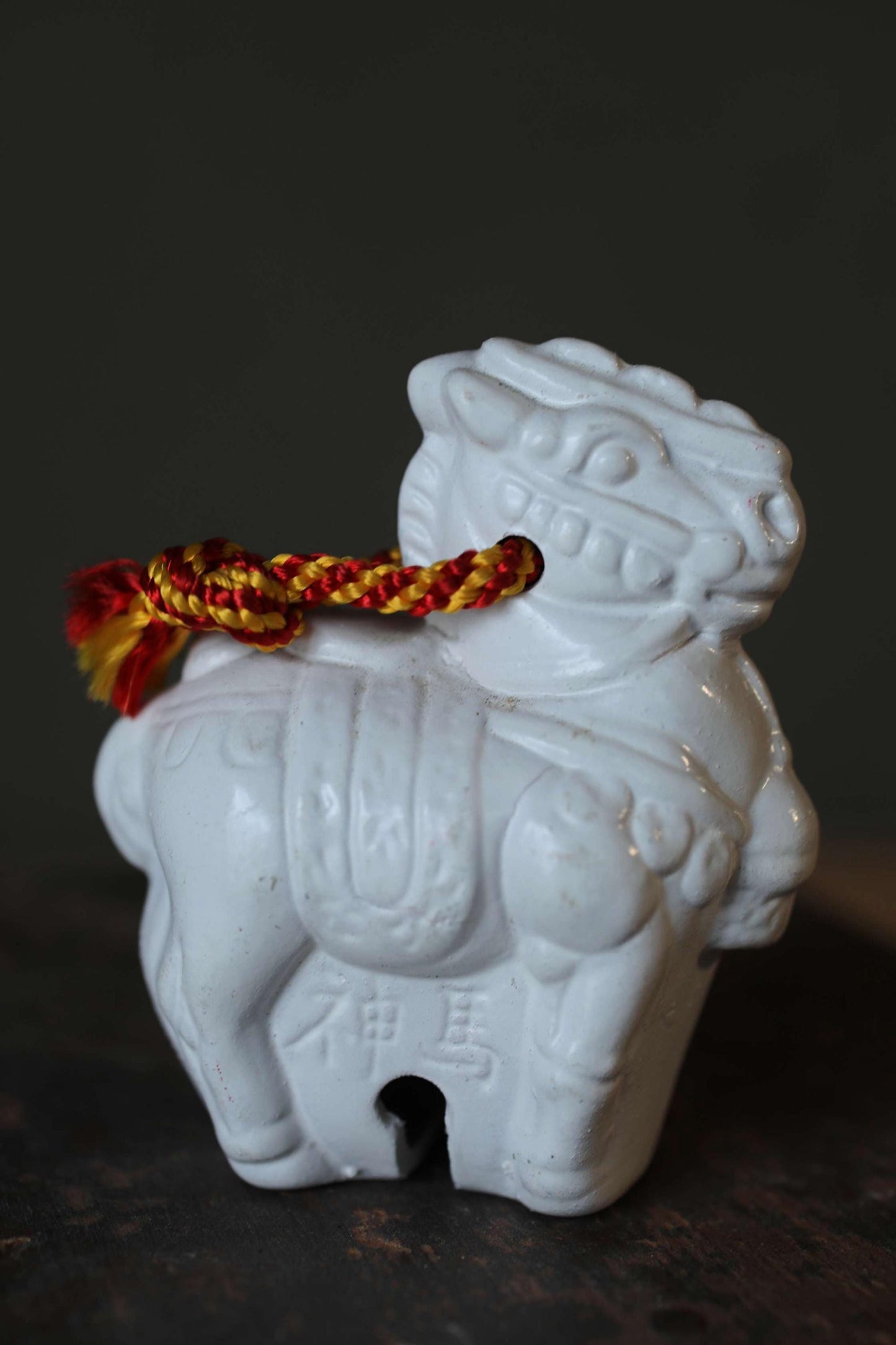 A white ceramic lion figurine with a red and yellow tassel attached to it.