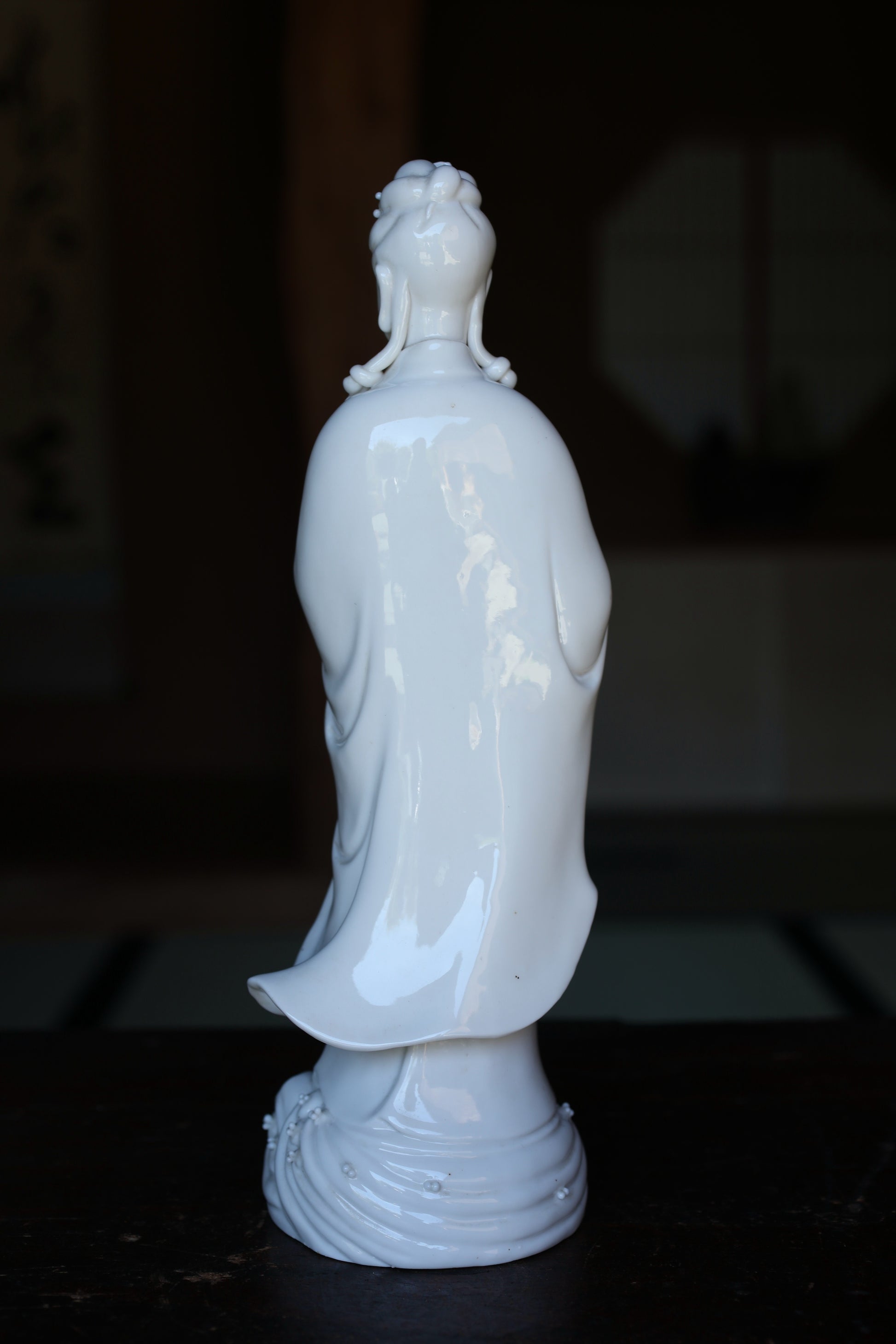 A white ceramic figurine of a person, possibly a deity, is displayed on a dark surface.