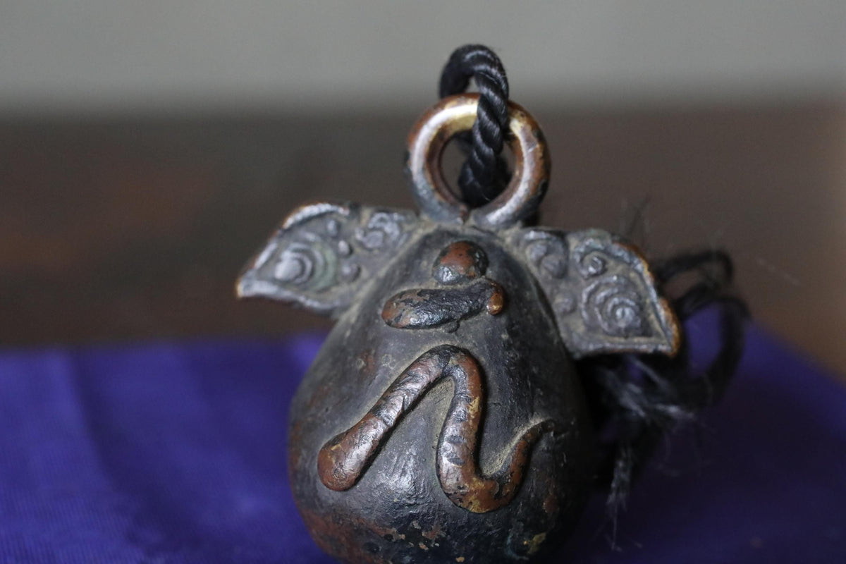 An antique metal bell with a snake design on it, hanging from a rope.