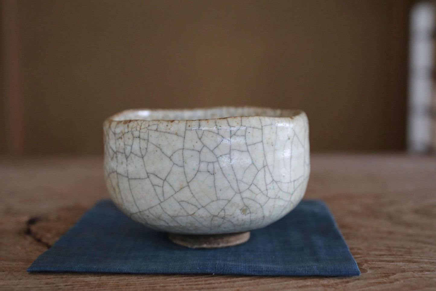 A white ceramic bowl with a cracked texture sits on a blue cloth on a wooden surface.