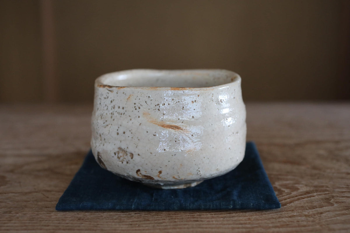 A white ceramic bowl with a textured surface sits on a dark blue cloth on a wooden surface.