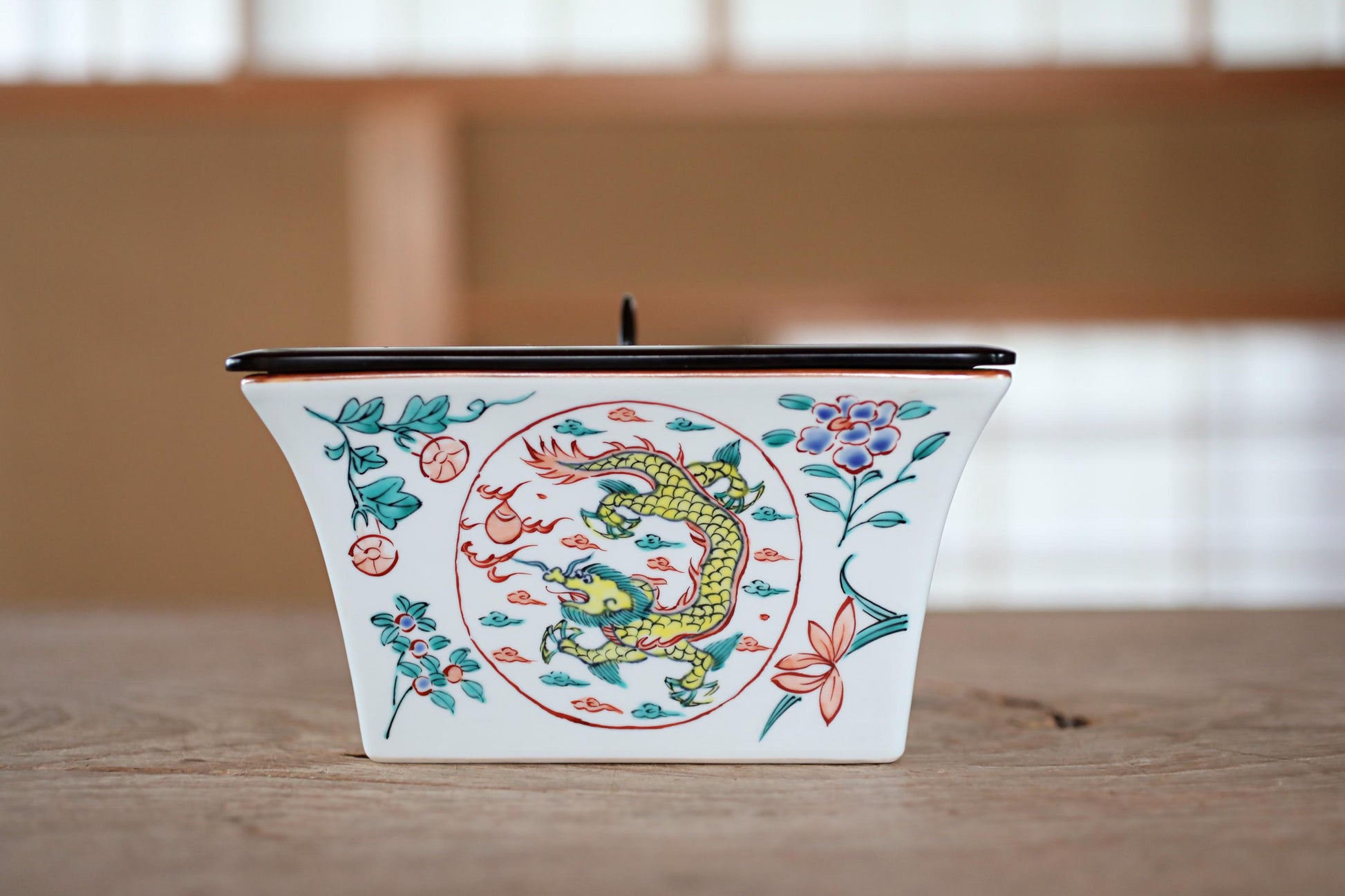 A ceramic container with a dragon design on it, placed on a wooden surface.