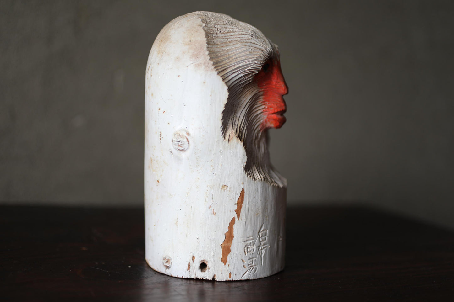 A white wooden sculpture of a monkey's head with red markings on its face and neck.