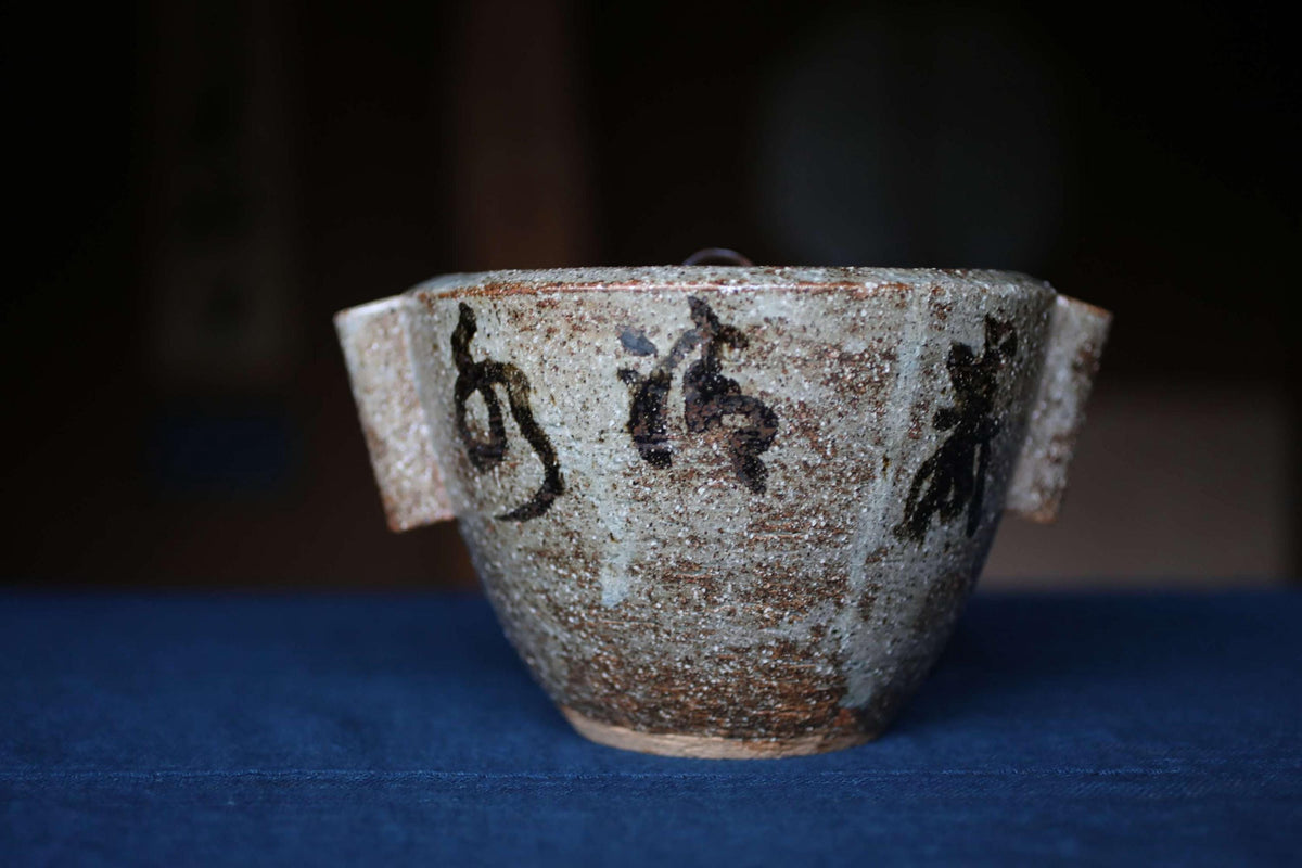 A ceramic bowl with a textured surface and two handles, sitting on a blue surface.