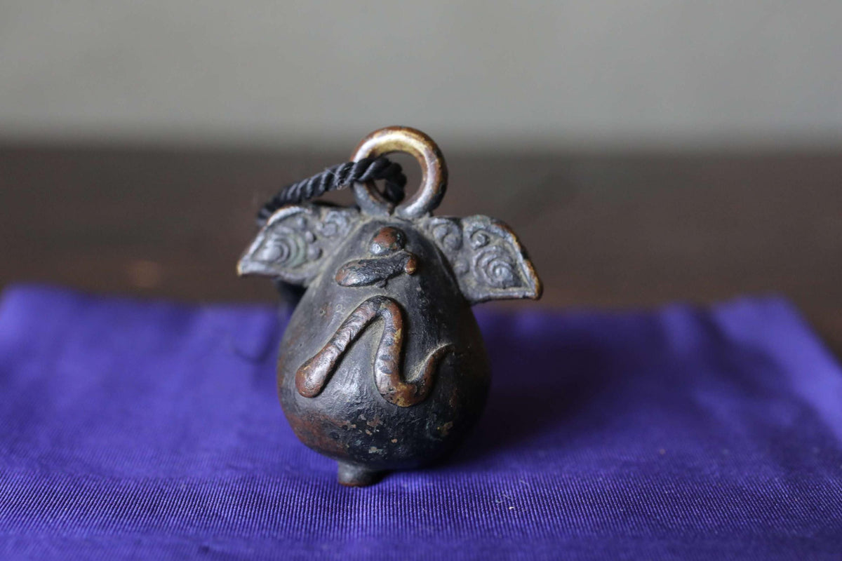 A decorative metal bell with an elephant-like design sits on a blue cloth.