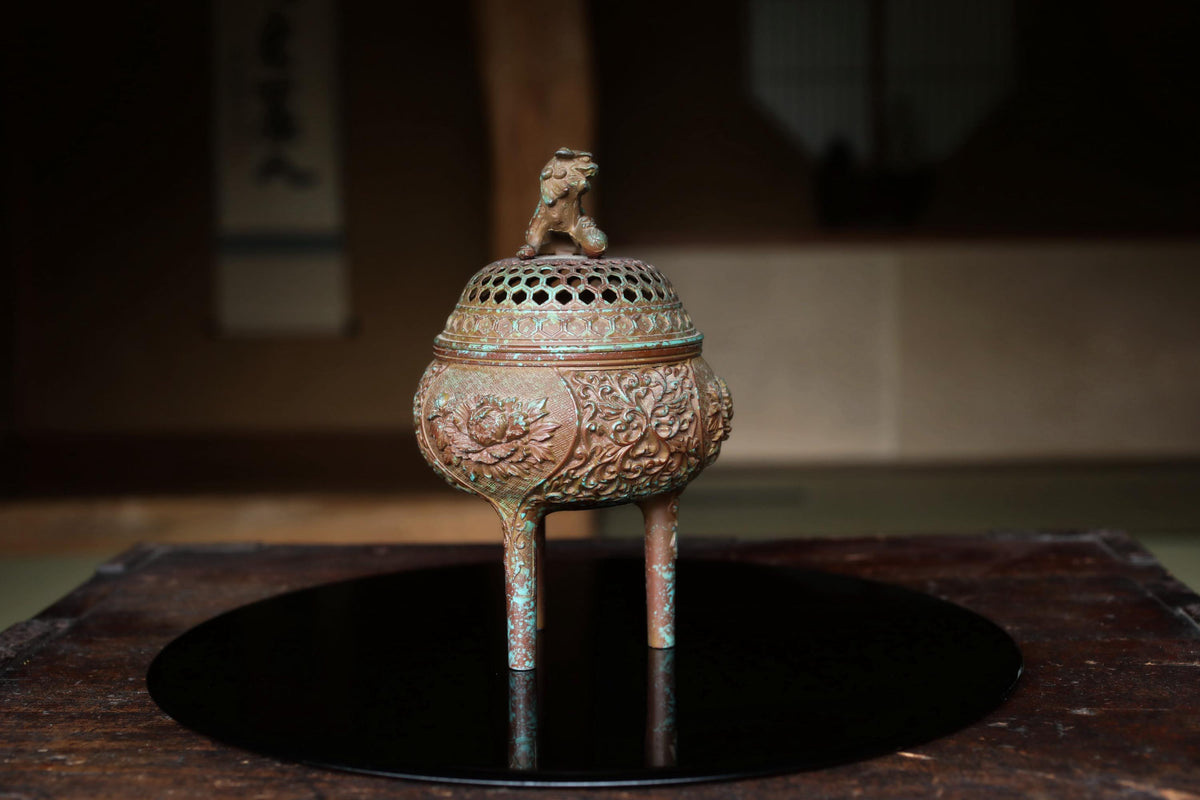 An ornate bronze incense burner with a lion figure on top, placed on a black circular tray.