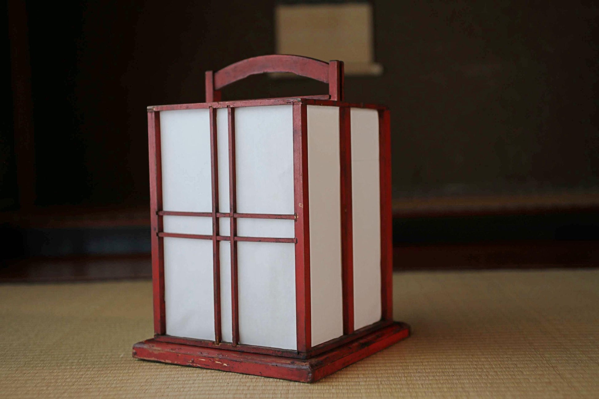A red lantern with white panels sits on a wooden surface, creating a warm and inviting atmosphere.