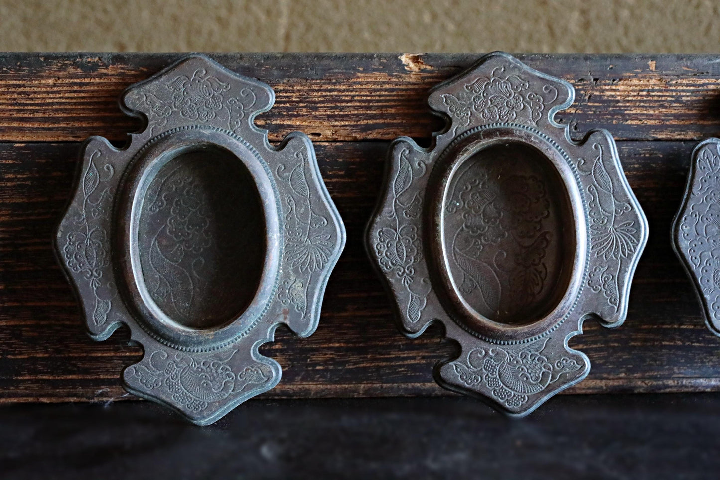 two ornate, antique-looking metal pieces with intricate designs, mounted on a wooden surface.