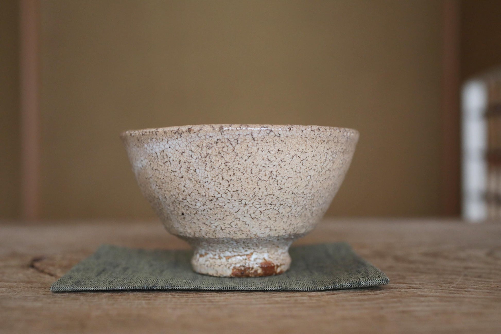 A white ceramic bowl with a speckled texture sits on a green cloth on a wooden surface.