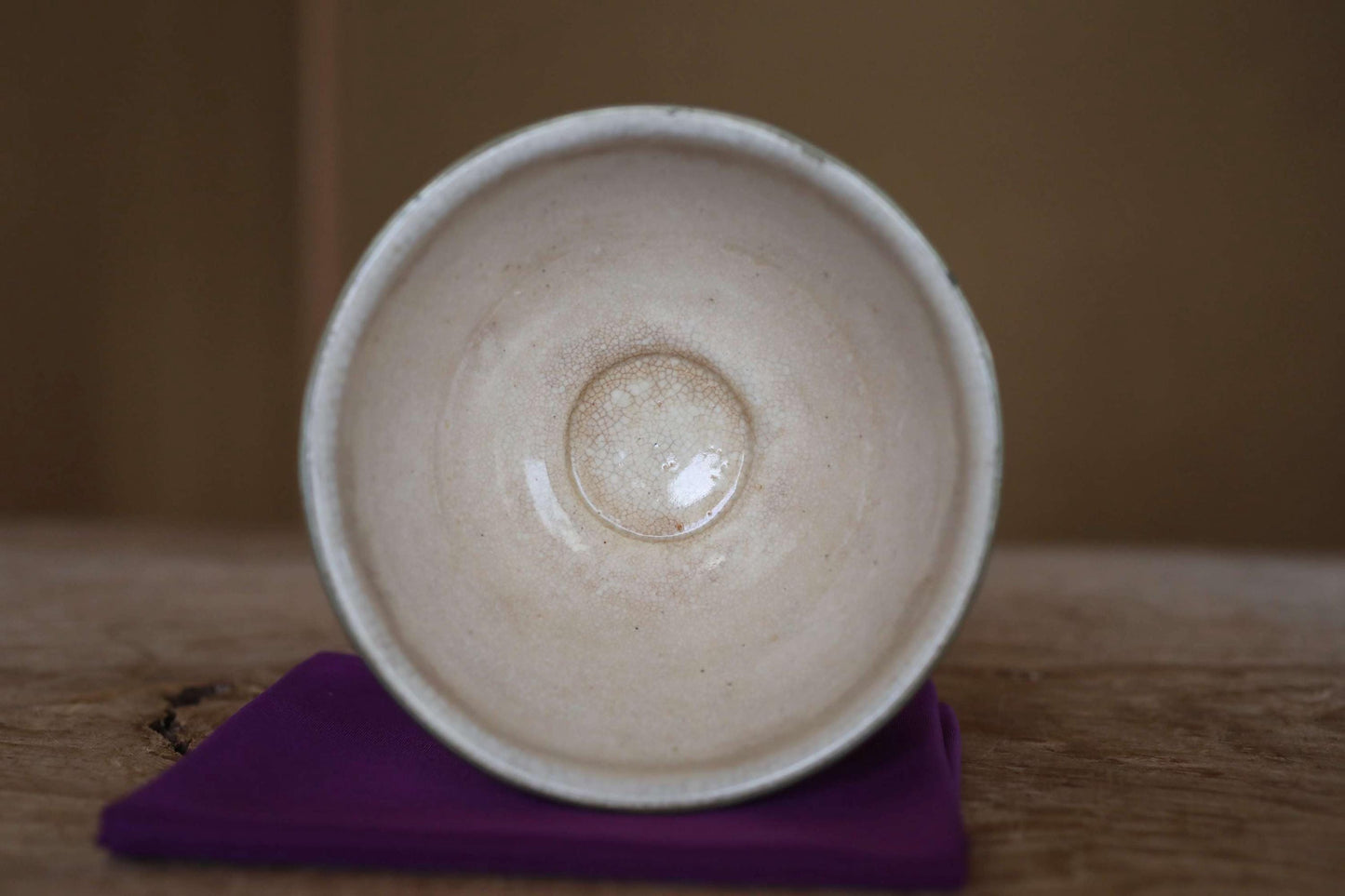 A white ceramic bowl with a small hole in the center, placed on a purple cloth on a wooden surface.