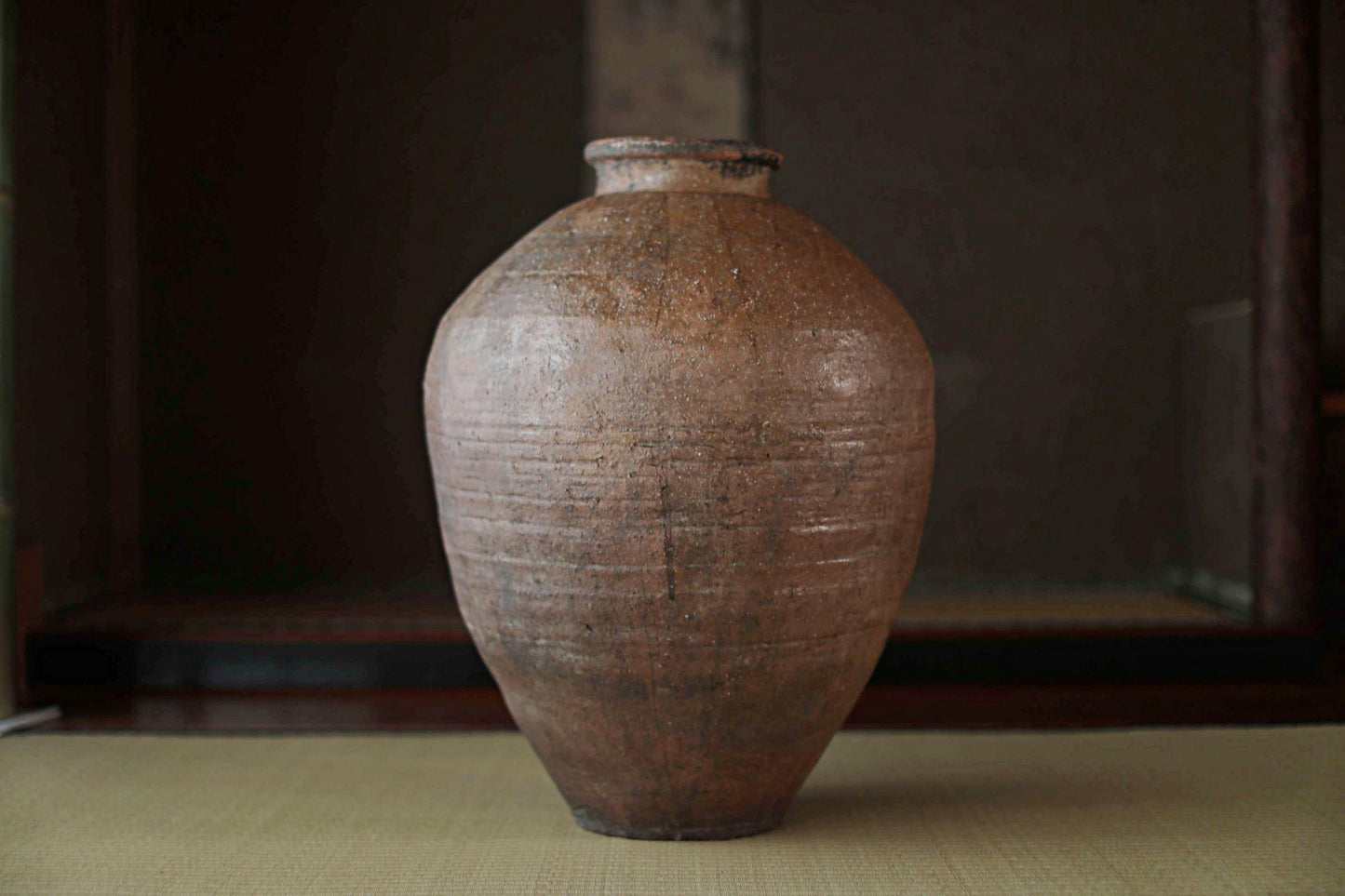 An old, weathered clay vase with a round shape and a narrow neck, sitting on a surface.