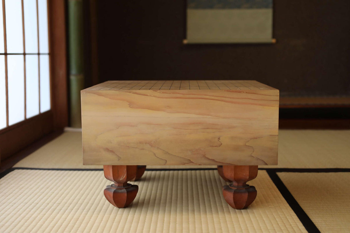 A wooden table with a checkerboard pattern on its surface, placed on a tatami mat in a room with a window and a painting on the wall.