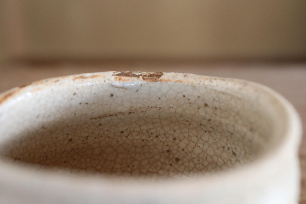 A close-up view of a white ceramic mug with a textured surface, showing signs of wear and tear.