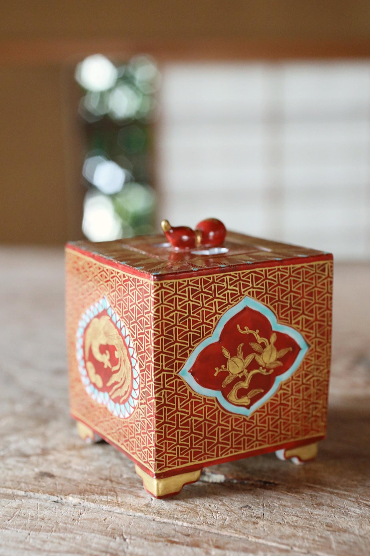 A red and gold decorative box with intricate patterns and designs, placed on a wooden surface.