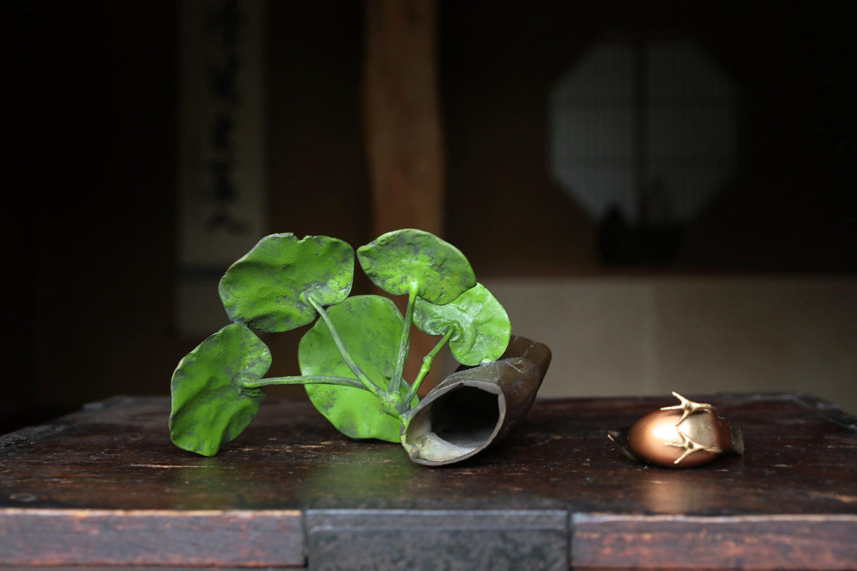 a wooden table with a plant, a small object, and a window in the background.