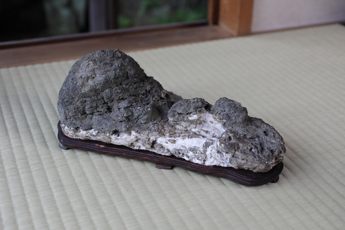 A large, irregularly shaped rock sits on a wooden stand, placed on a woven mat.