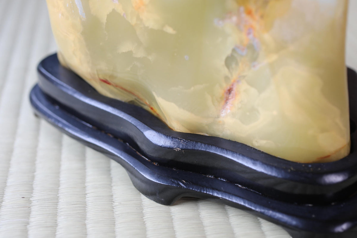 a close-up view of a yellowish-green stone or gemstone, possibly a piece of amber or amberite, placed on a black stand or base.