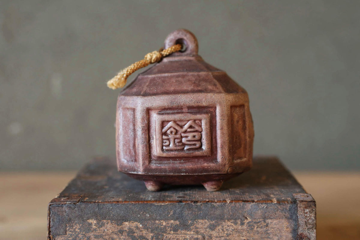 A small, brown ceramic bell with a decorative design on its side, sitting on a wooden surface.