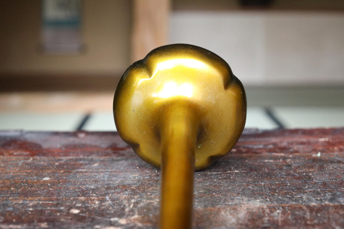 A close-up view of a golden-colored metal object, possibly a candlestick or a similar item, resting on a wooden surface.
