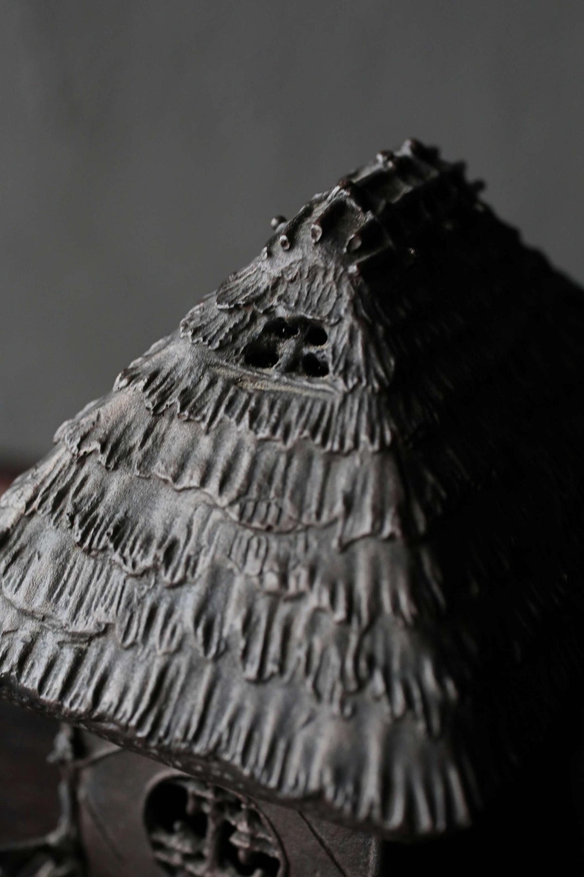 A close-up view of a dark, textured metal sculpture resembling a house or building with a pointed roof and intricate details.