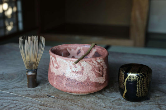 a pink ceramic bowl with a wooden stick, a black ceramic box, and a wooden brush on a wooden surface.