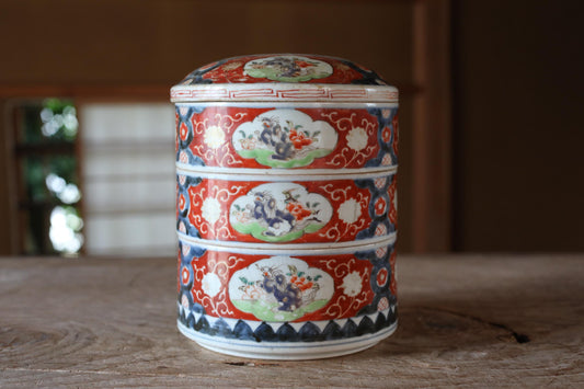 A decorative ceramic container with a floral pattern and a red and white color scheme, placed on a wooden surface.