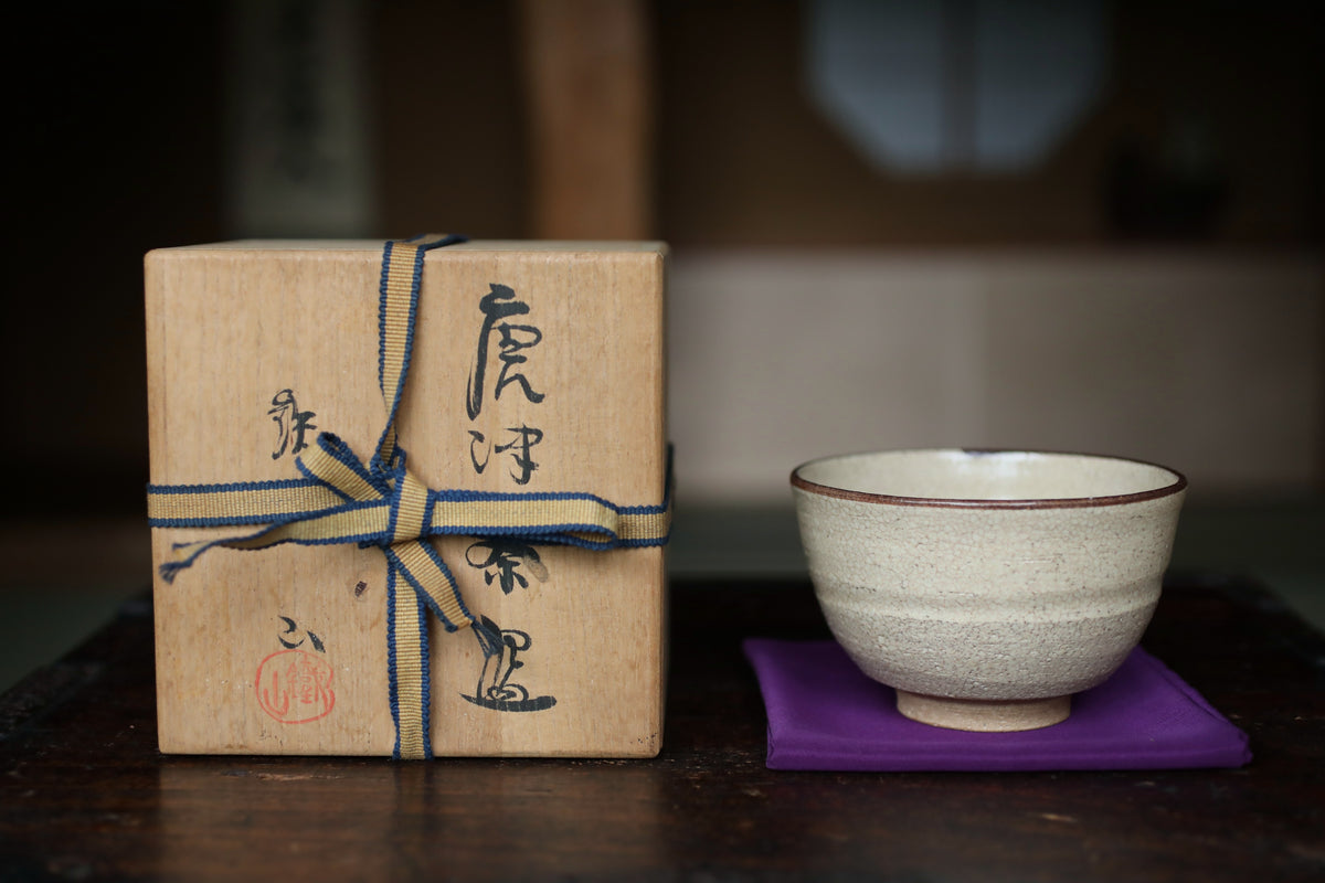 a wooden box with Japanese characters tied around it, and a white ceramic bowl placed on a purple coaster on a wooden table.