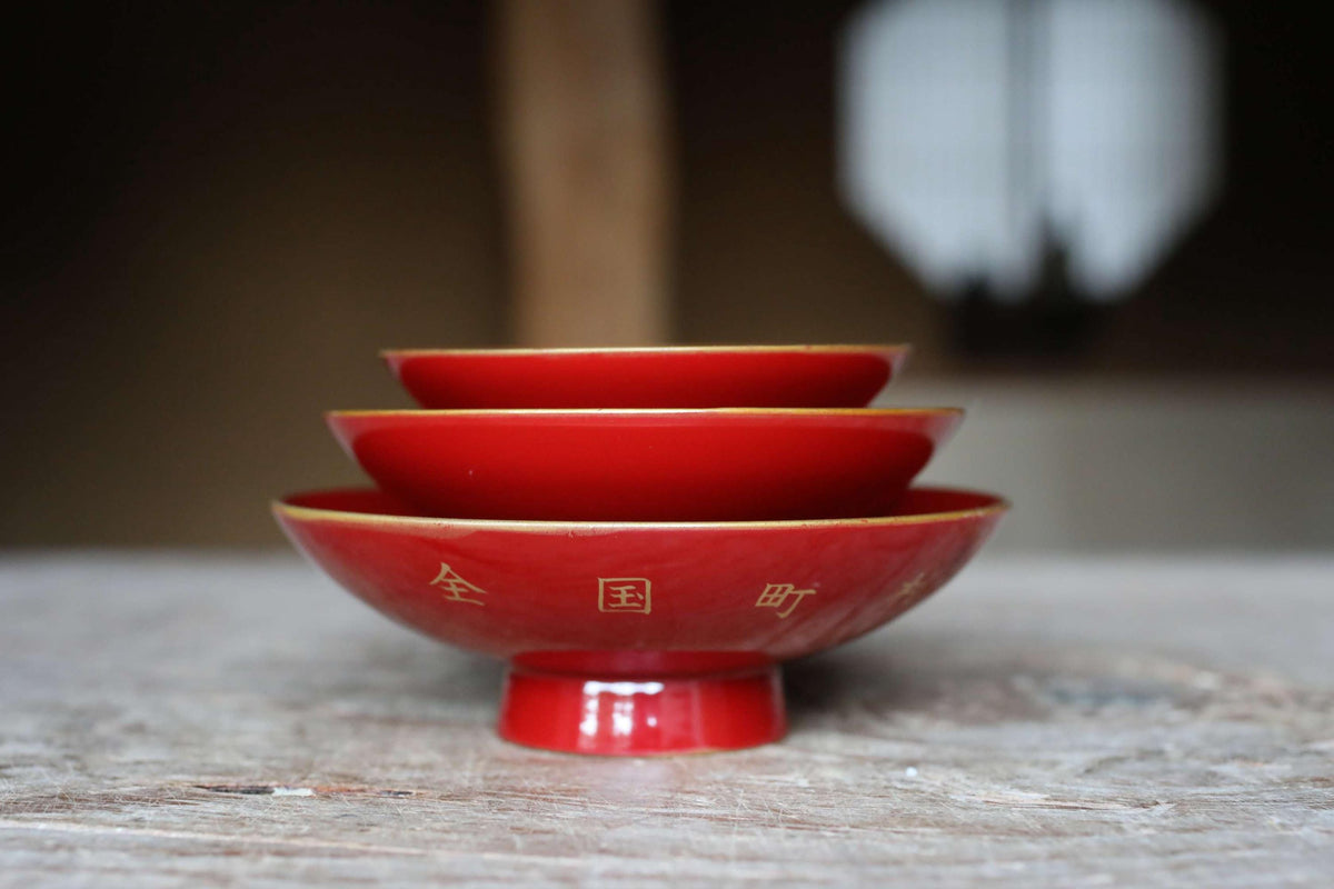 A stack of three red bowls with gold accents, placed on a wooden surface.
