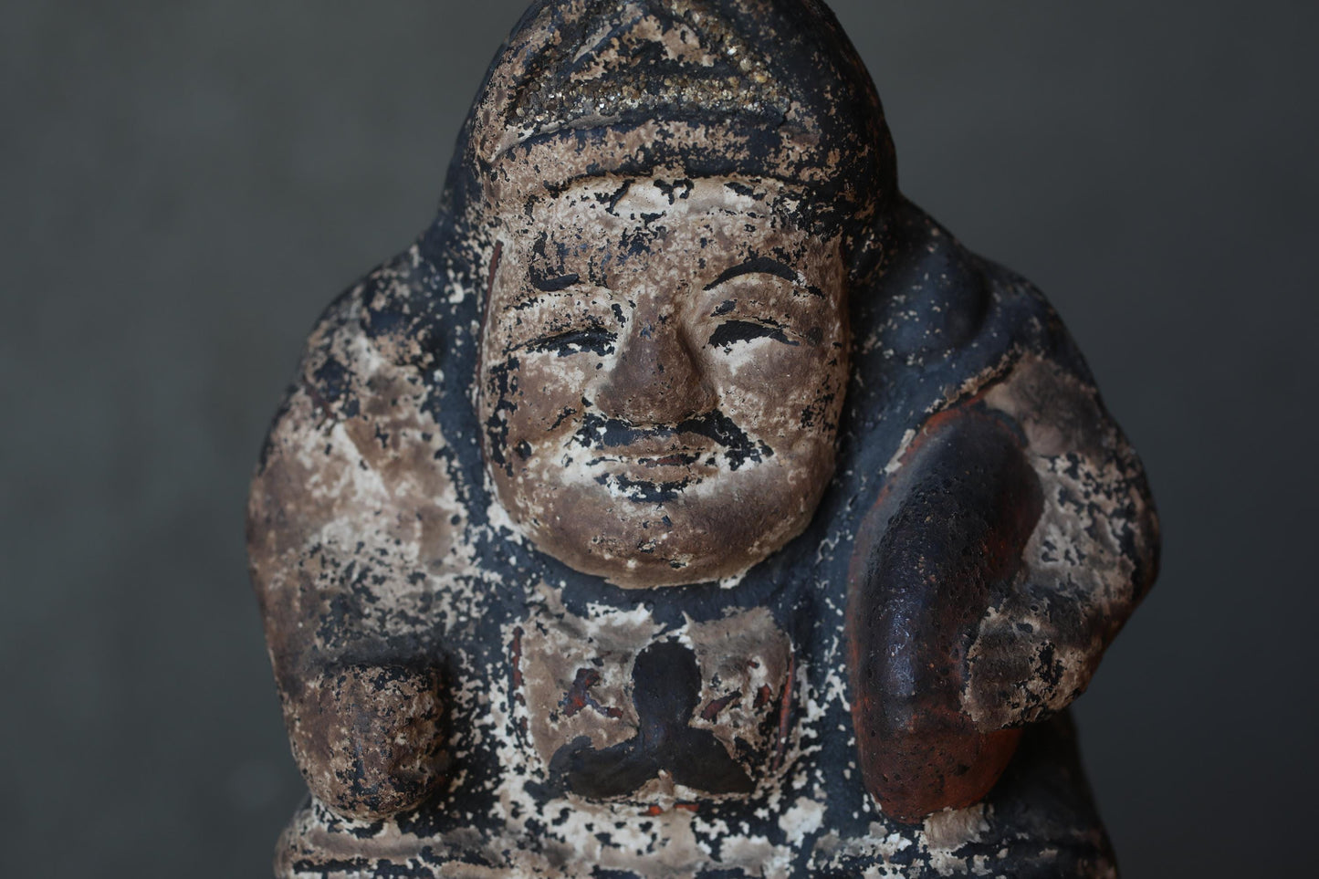 An old, weathered statue of a man with a serious expression, possibly a religious figure, against a dark background.