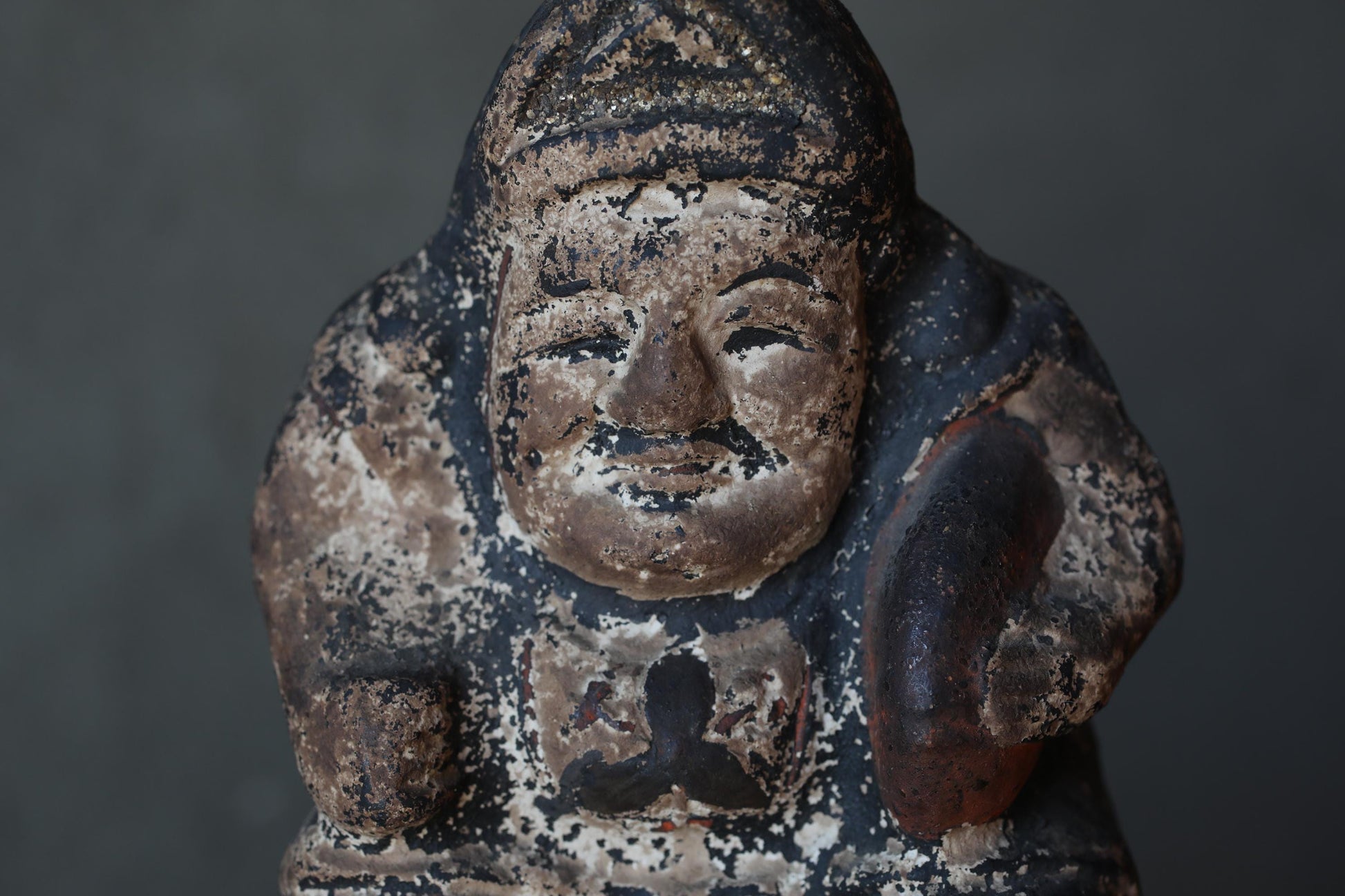 An old, weathered statue of a man with a serious expression, possibly a religious figure, against a dark background.