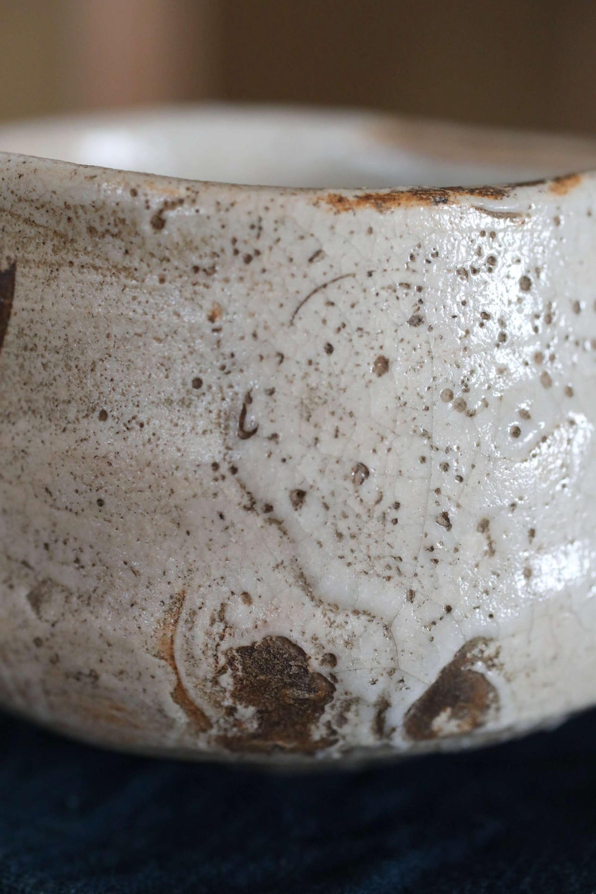 A close-up image of a white ceramic bowl with a textured surface, featuring small brown spots and a rough, uneven appearance.