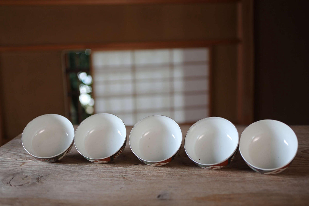 A row of five white bowls with intricate designs on their rims is arranged on a wooden surface.