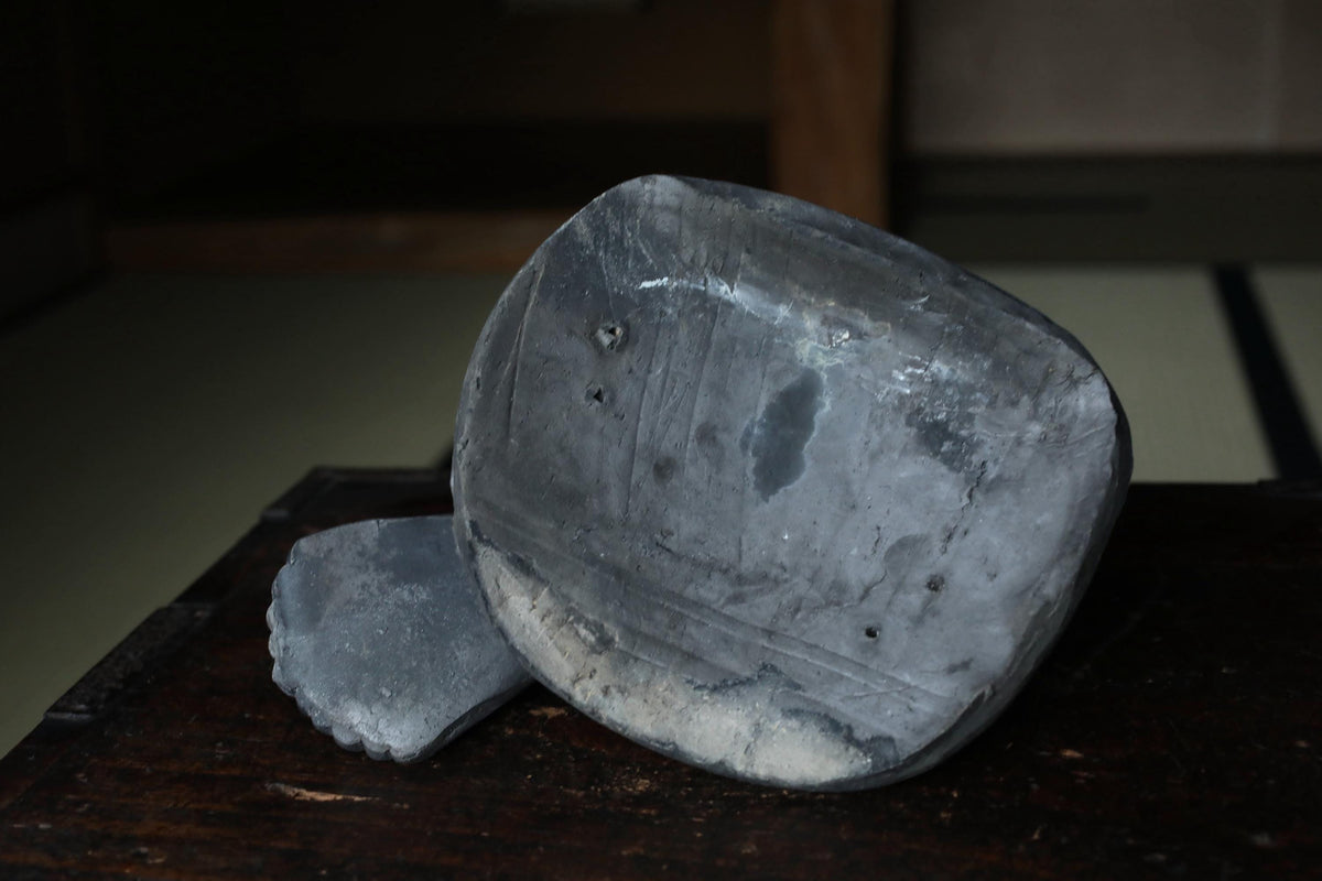 a close-up view of a dark gray, weathered object, possibly a piece of pottery or a stone, resting on a wooden surface.