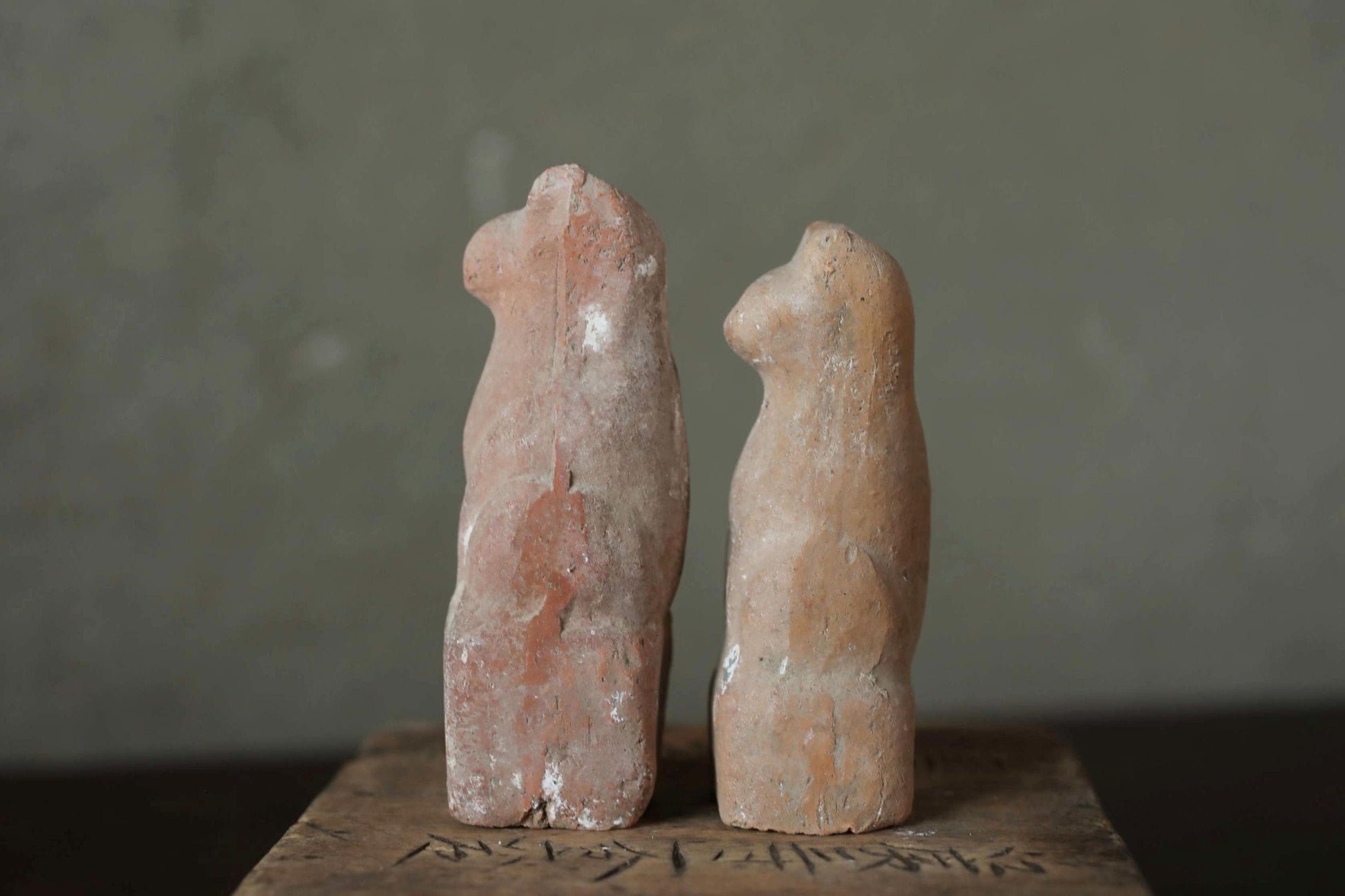 Two ancient clay figurines of cats, one larger and one smaller, standing side by side against a gray background.