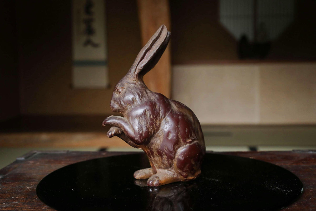 A bronze statue of a rabbit sitting on a black surface.