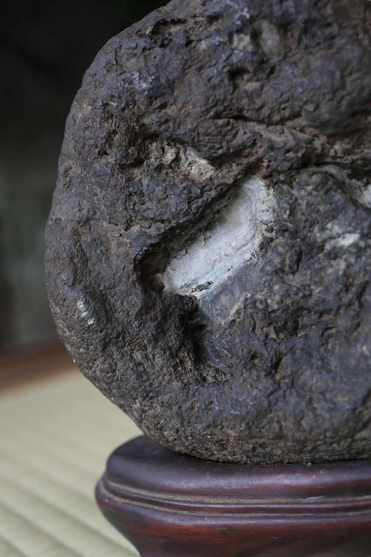 A close-up image of a large, dark rock with a hole in it, resting on a wooden base.