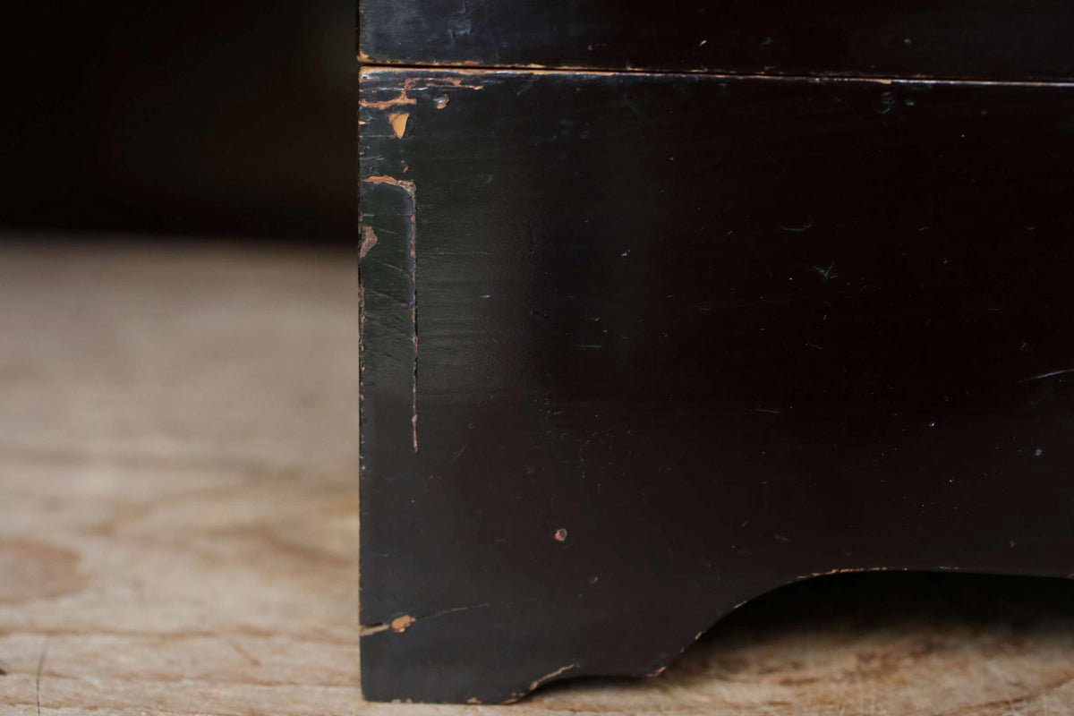 A close-up view of a dark wooden box or chest, with visible signs of wear and tear, such as peeling paint and a chipped edge.