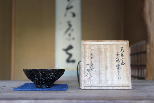 a black bowl and a wooden box with Japanese characters on it, placed on a wooden surface.