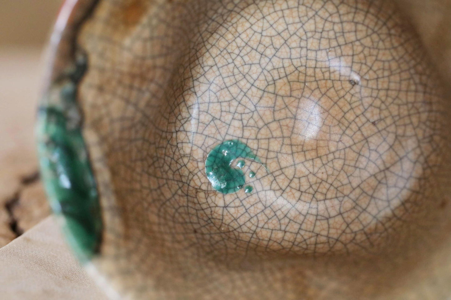 A close-up view of a ceramic bowl with a green and brown color scheme, featuring a cracked and textured surface.