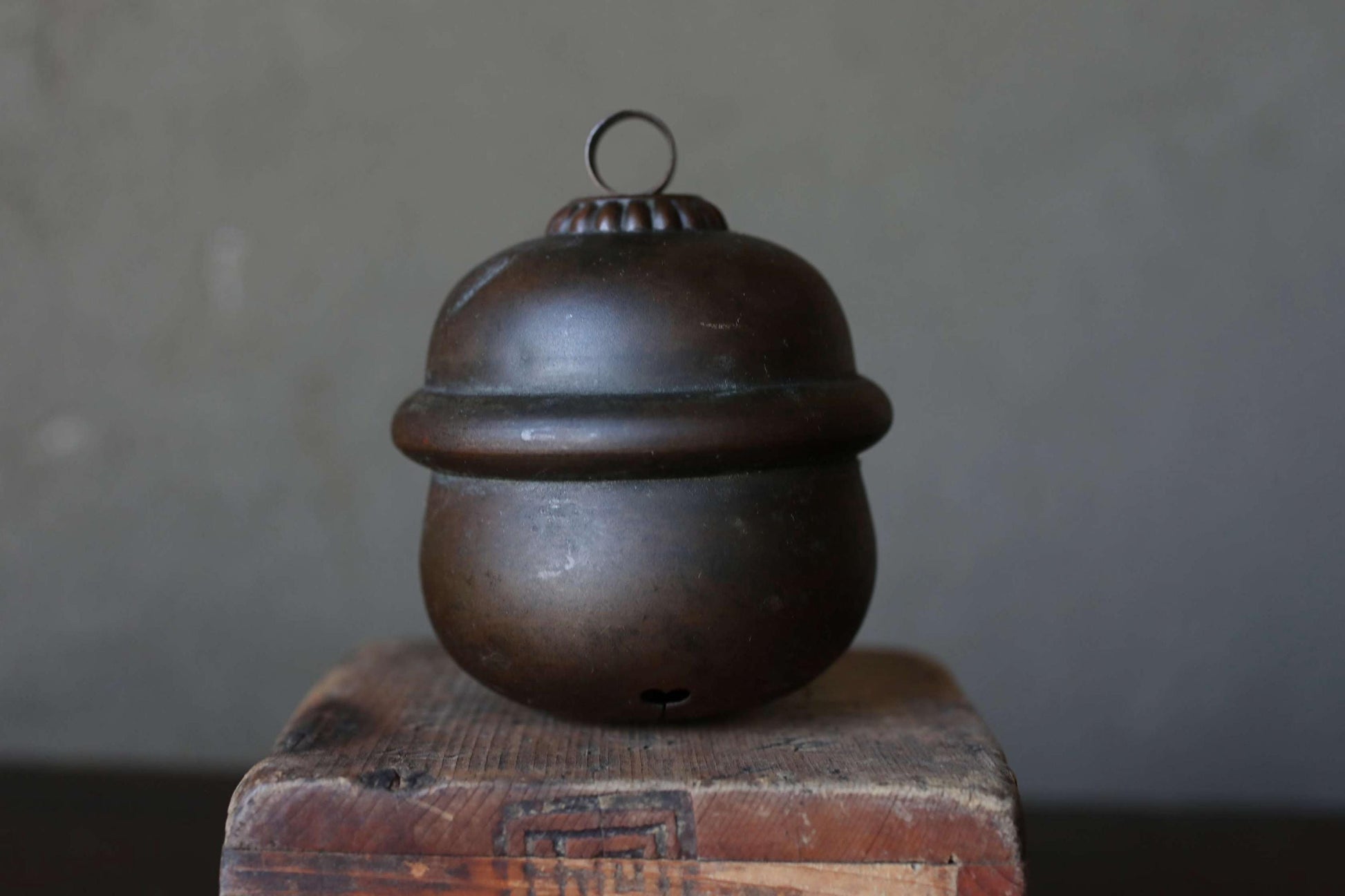 A dark brown, round metal container with a lid, sitting on a wooden surface against a gray background.