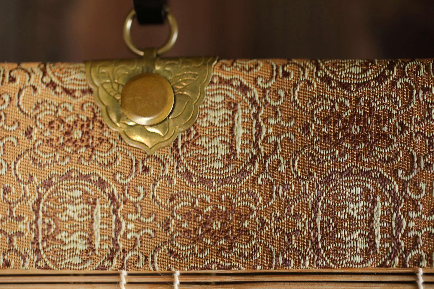 a close-up view of a decorative fabric with a gold-colored metal clasp or clasp-like element attached to it.