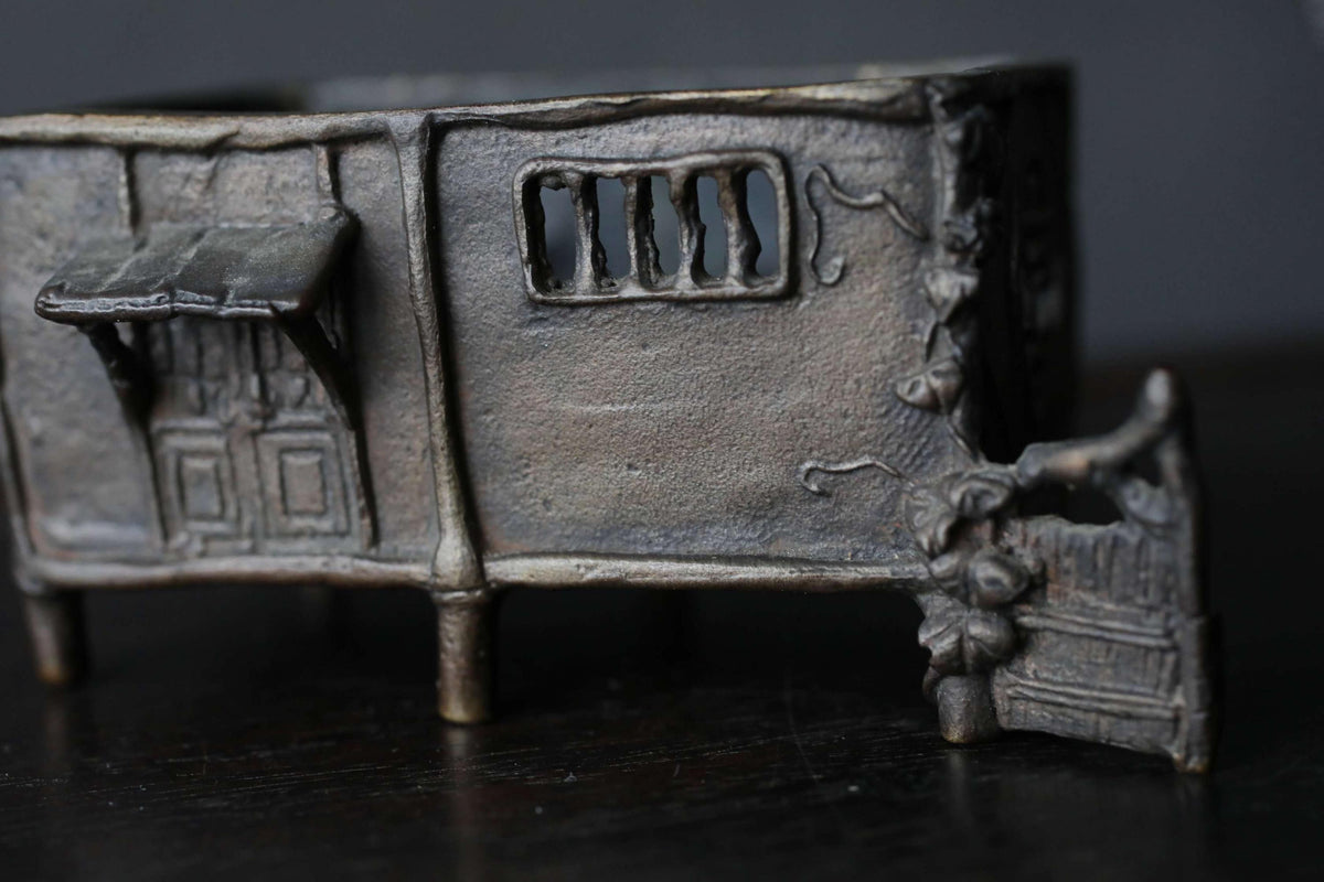 A close-up image of a metal sculpture depicting a house with a door and window.