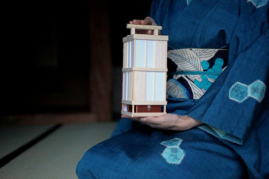 A person wearing a blue kimono holds a wooden lantern in their hand.