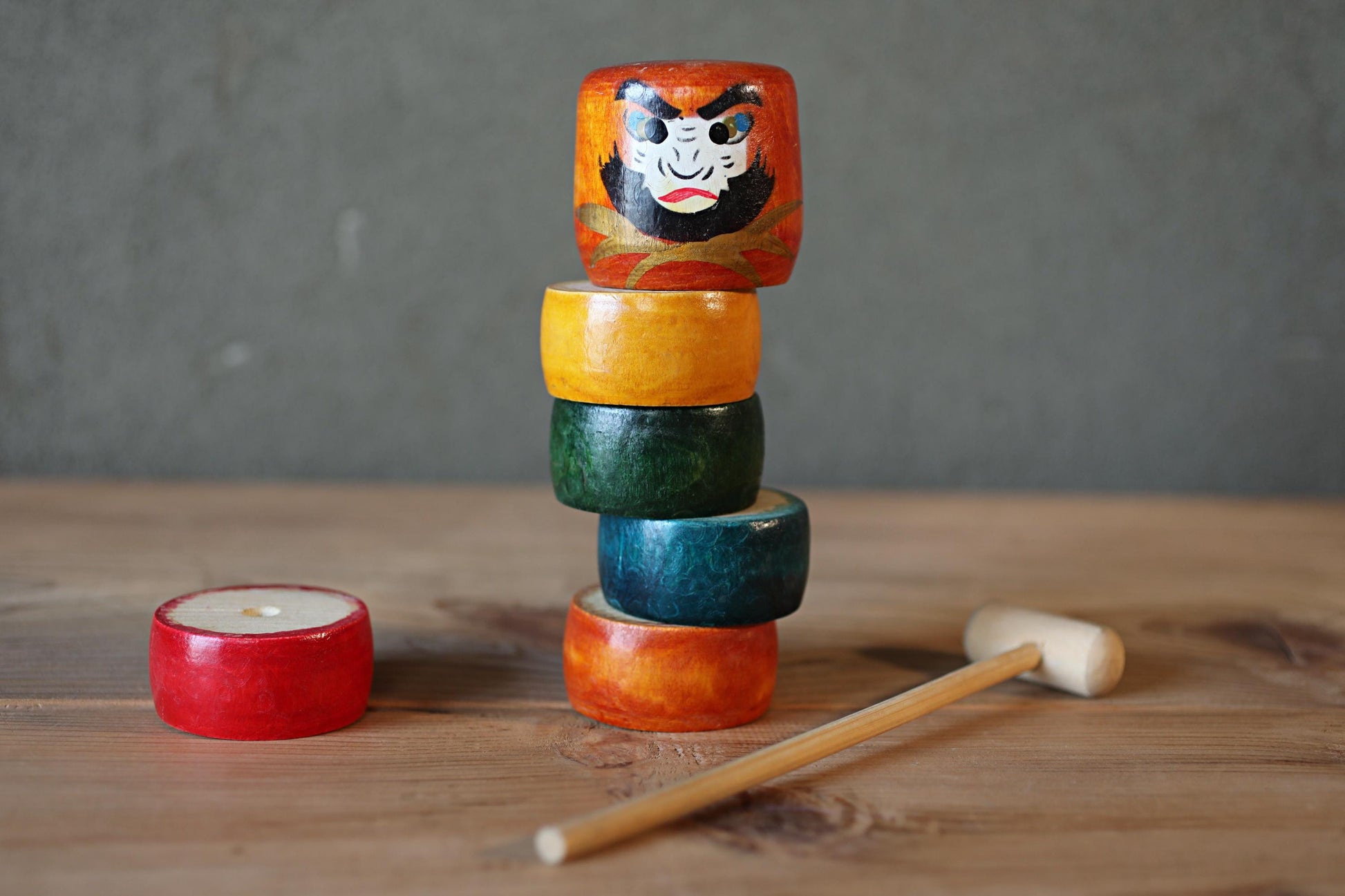 A stack of colorful wooden dolls with painted faces and a wooden mallet on a wooden surface.