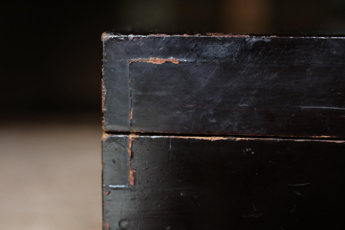 A close-up view of a dark wooden surface with visible signs of wear and tear, including peeling paint and a rough texture.