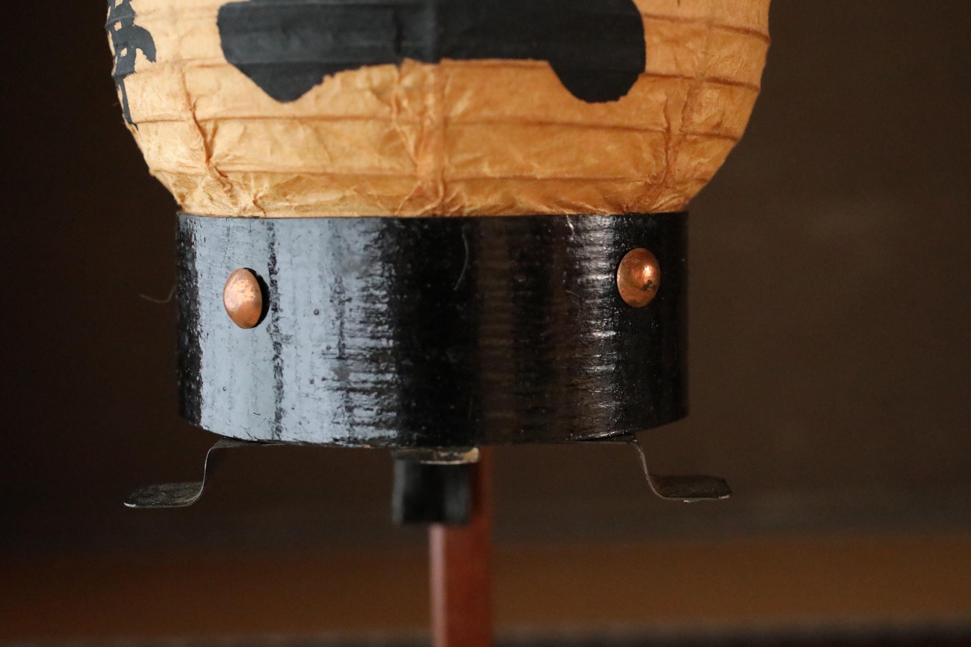 A close-up view of a decorative paper lantern with a black and gold design, featuring a black base with two copper-colored screws.