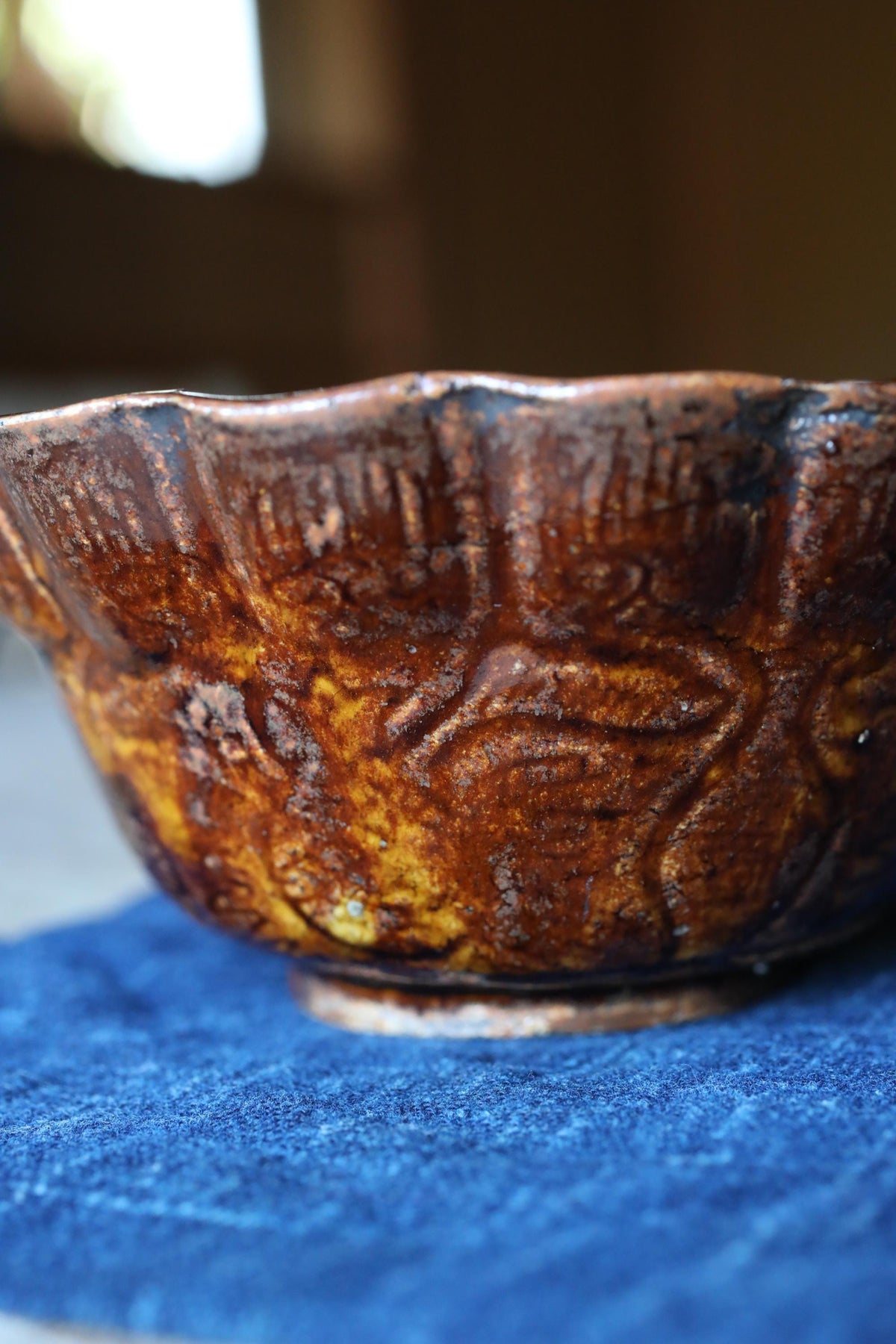 A close-up image of a brown ceramic bowl with a scalloped edge, resting on a blue surface.